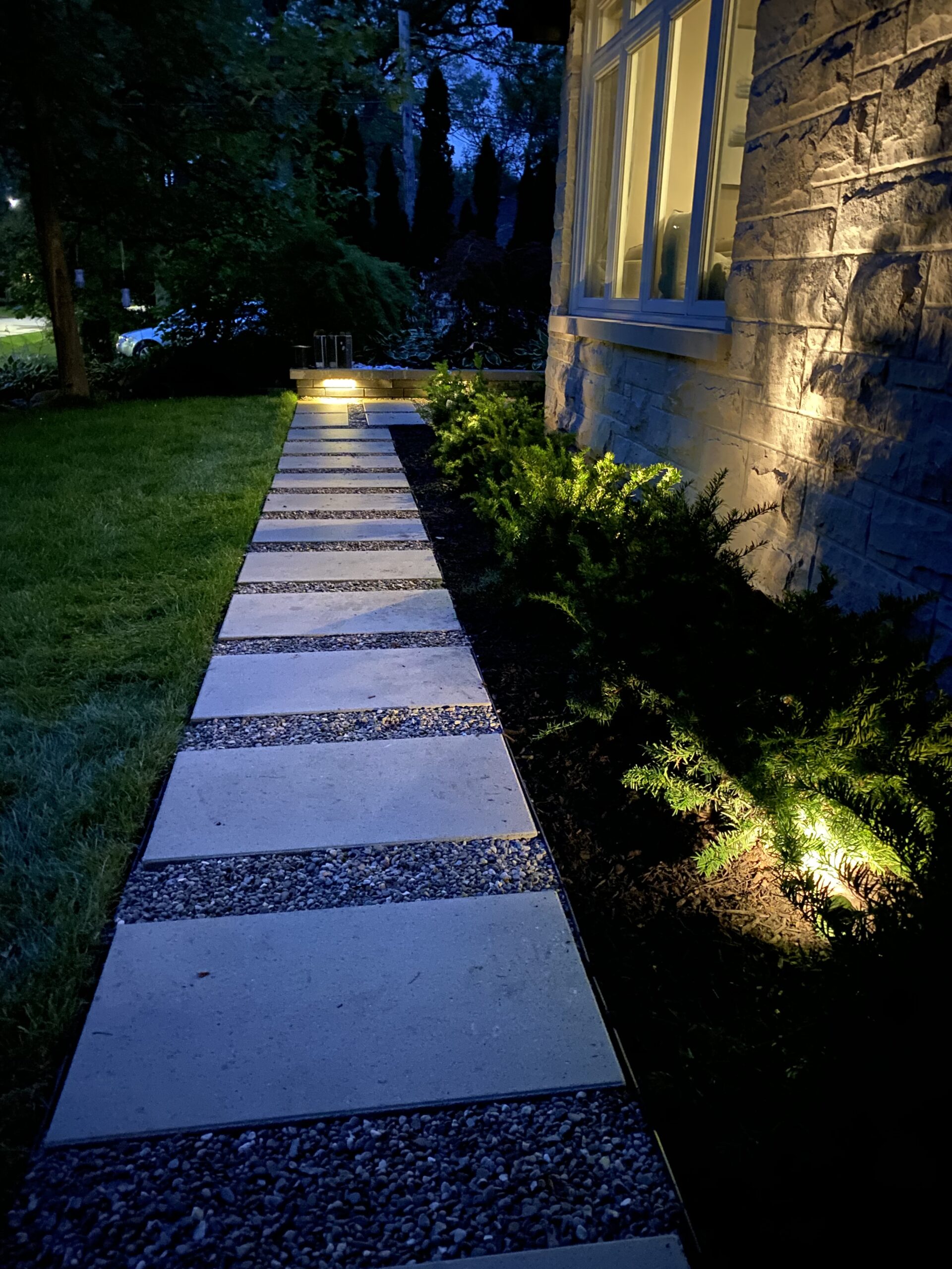 Large rectangular stepping stones with gravel joints and garden lighting beside a stone home