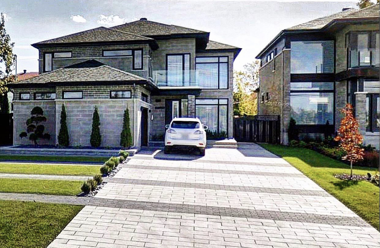 Wide interlocking paver driveway leading to a modern home with dark garage doors