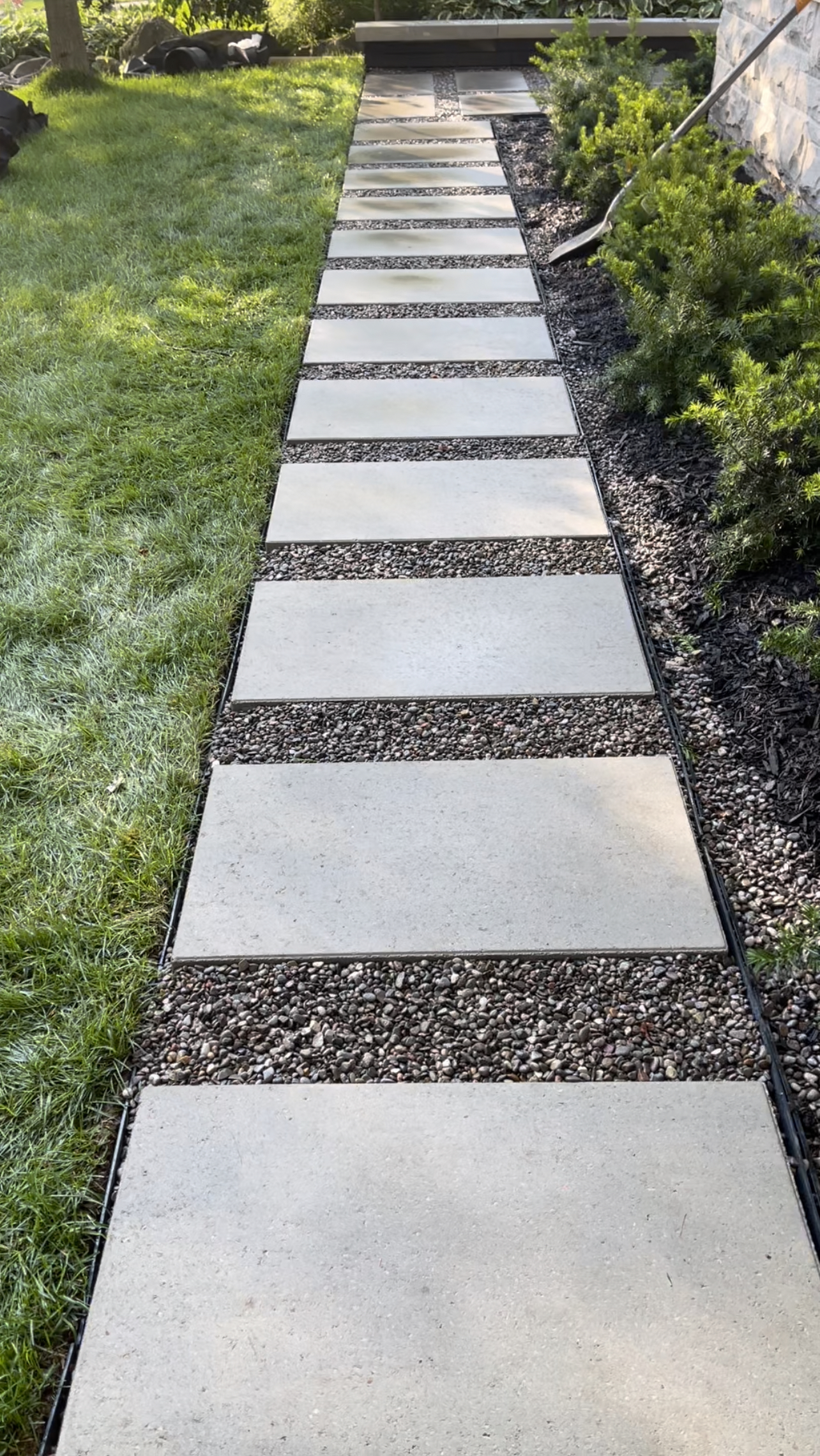 Large pale stepping stones set in gravel between lawn and planted garden beds