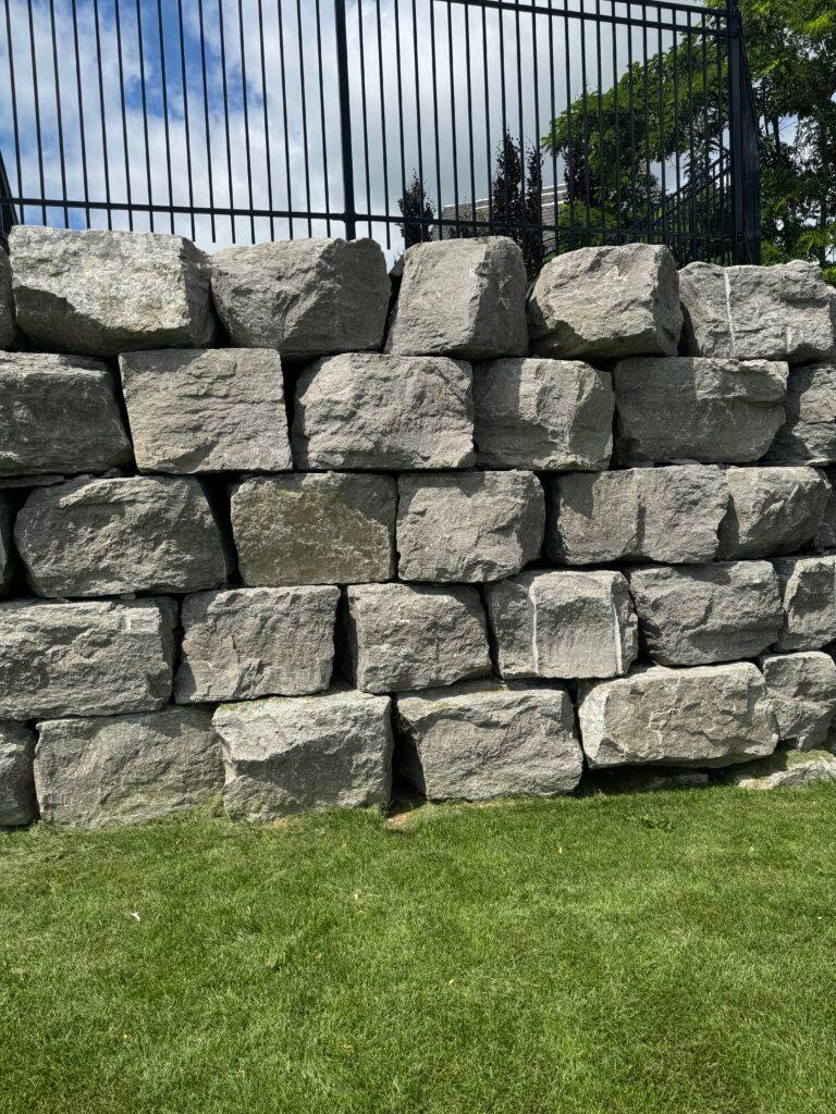Armour stone retaining wall with natural weathered limestone blocks stacked in irregular courses behind metal railings.