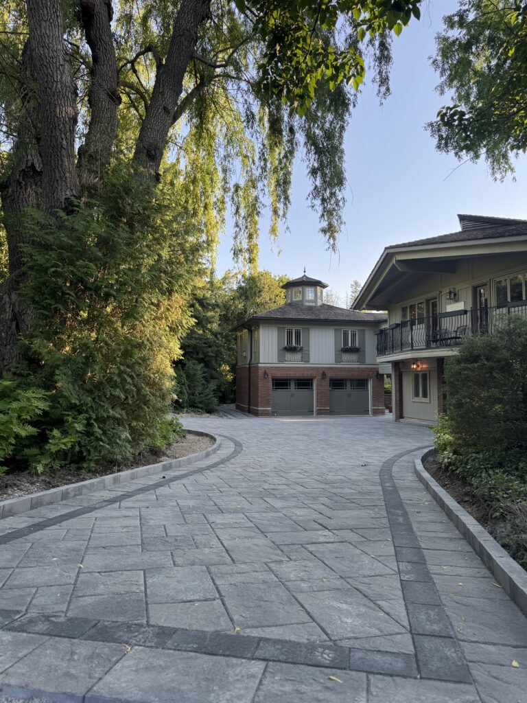 Large grey paver driveway with curved border edging leading to brick and timber two-story garage with cupola