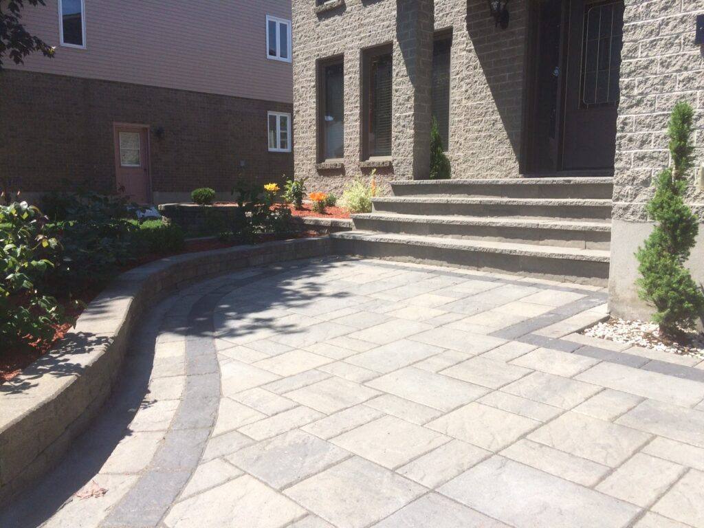 Stone patio with rectangular pavers, curved retaining wall planter, and wide stone steps leading to building entrance.